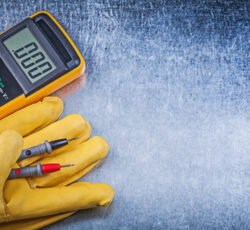 Digital,electric,tester,safety,gloves,on,metallic,background,electricity,concept.